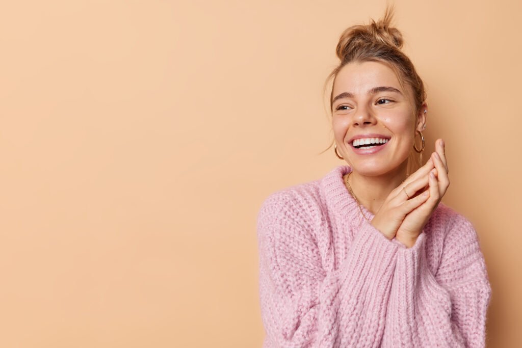 Smiling woman in a pink sweater looking to the side with a joyful and relaxed expression, symbolizing healing and renewed confidence after a breakup.
