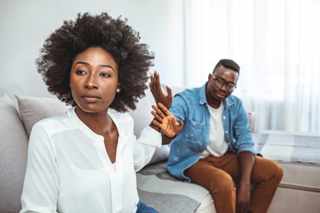 Woman raising her hand to create distance while sitting with her partner, showing emotional tension and a need for space in the relationship.