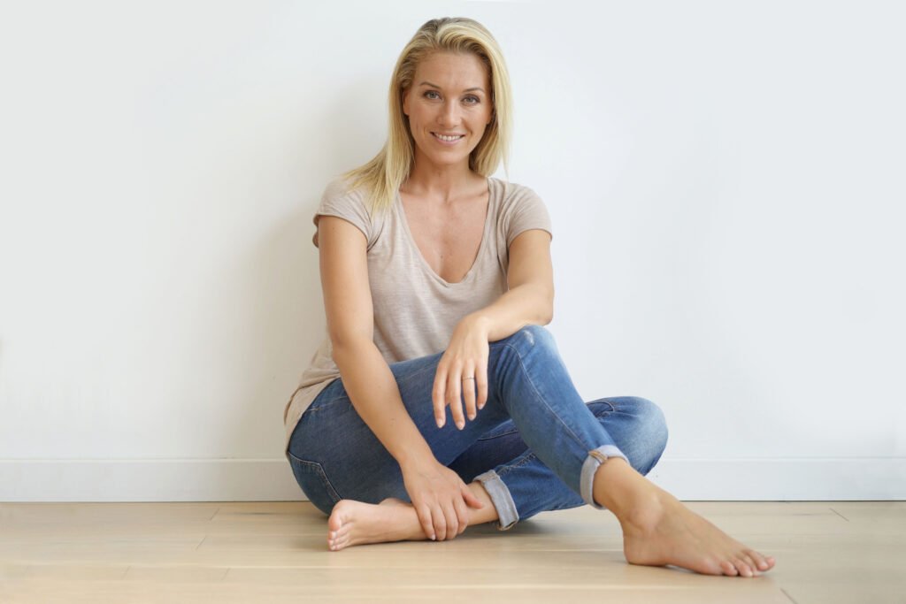 Woman sitting on the floor with a calm smile, looking relaxed and grounded as she reconnects with herself after emotional growth.
