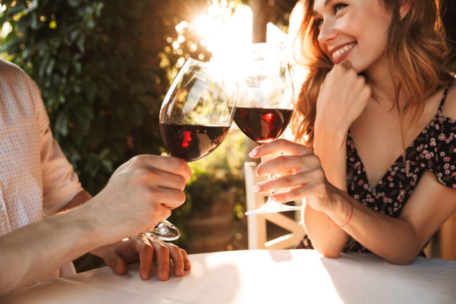 A woman in a stylish first date outfit smiling while toasting wine with her date during a romantic dinner at sunset.