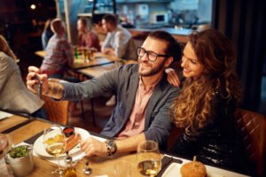First date outfit: A couple takes a warm selfie at dinner, her in a chic black top and him in a smart button-down, showcasing how the right clothes create a confident, connected vibe.