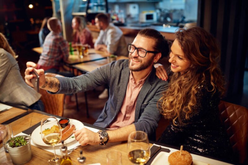 First date outfit: A couple takes a warm selfie at dinner, her in a chic black top and him in a smart button-down, showcasing how the right clothes create a confident, connected vibe.