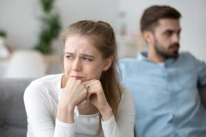 Woman trying to recover from a break up, sitting on a couch with a tissue while her partner avoids eye contact in the background.