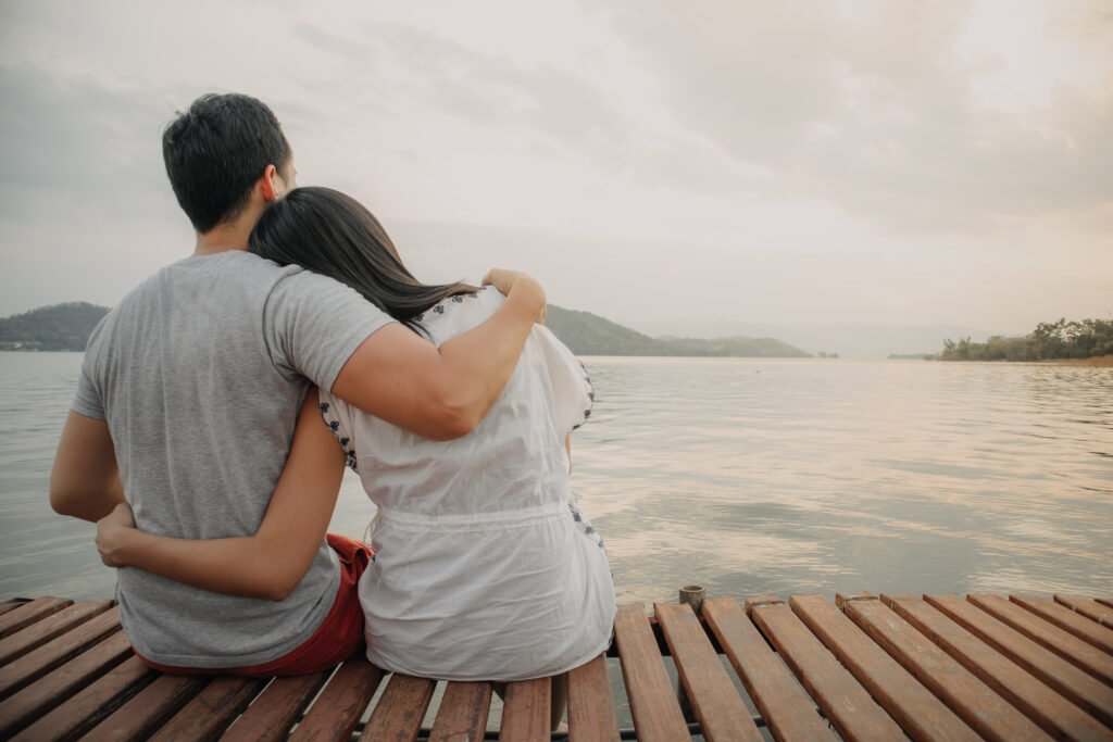 Couple happy in a relationship by the water with their arms around each other, enjoying a peaceful and intimate moment.