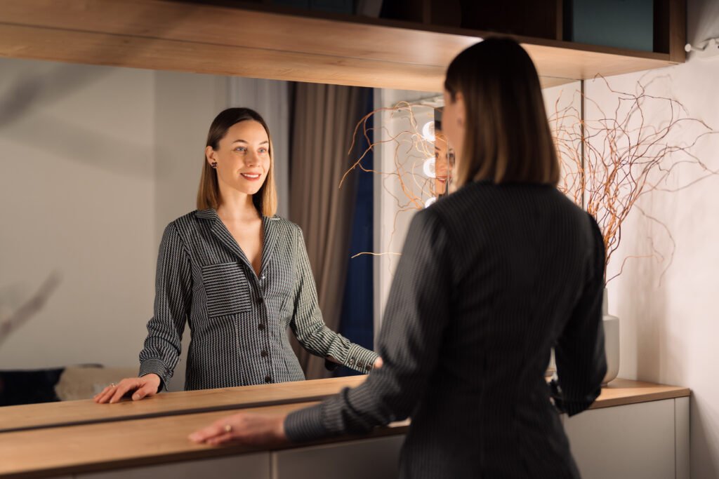Woman smiling at her reflection in the mirror, symbolizing self acceptance, confidence, and rediscovering her self worth