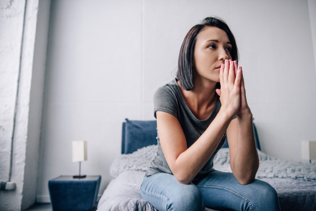 Woman sitting on the edge of her bed with her hands near her face, looking thoughtful and overwhelmed as she realizes she is losing herself in her relationship.