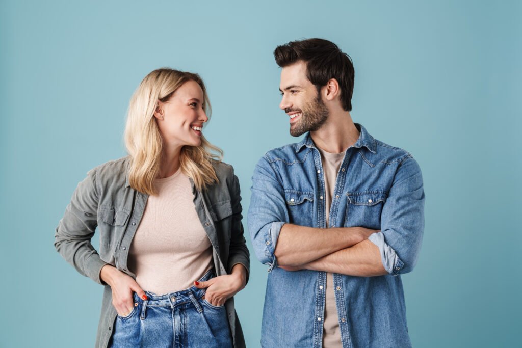 A smiling man and woman looking at each other with warmth and connection while standing against a blue background.