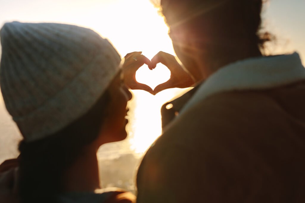 Couple forming a heart shape with their hands at sunset near the water