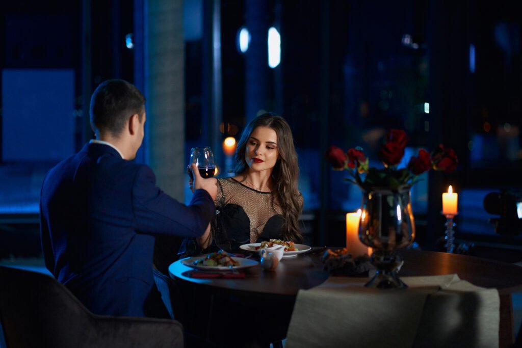 A man and woman toasting with wine during a romantic first date dinner in a dimly lit restaurant.
