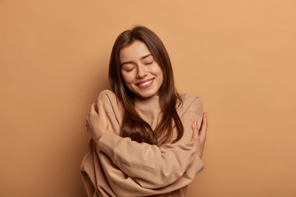 Woman hugging herself with eyes closed, expressing self-love, inner peace, emotional healing, and confidence.