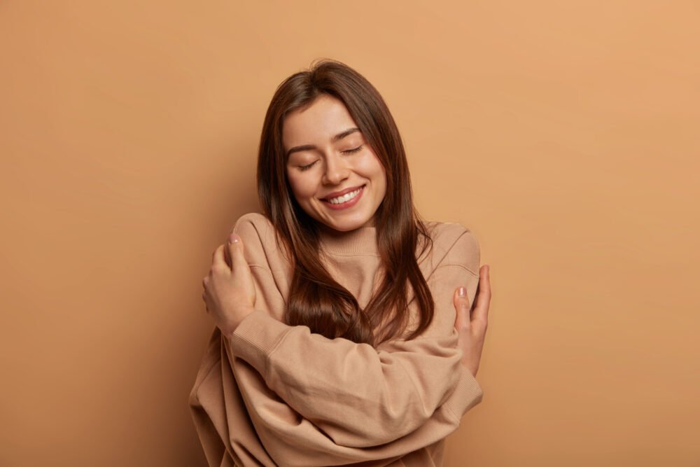 Woman hugging herself with eyes closed, expressing self-love, inner peace, emotional healing, and confidence.