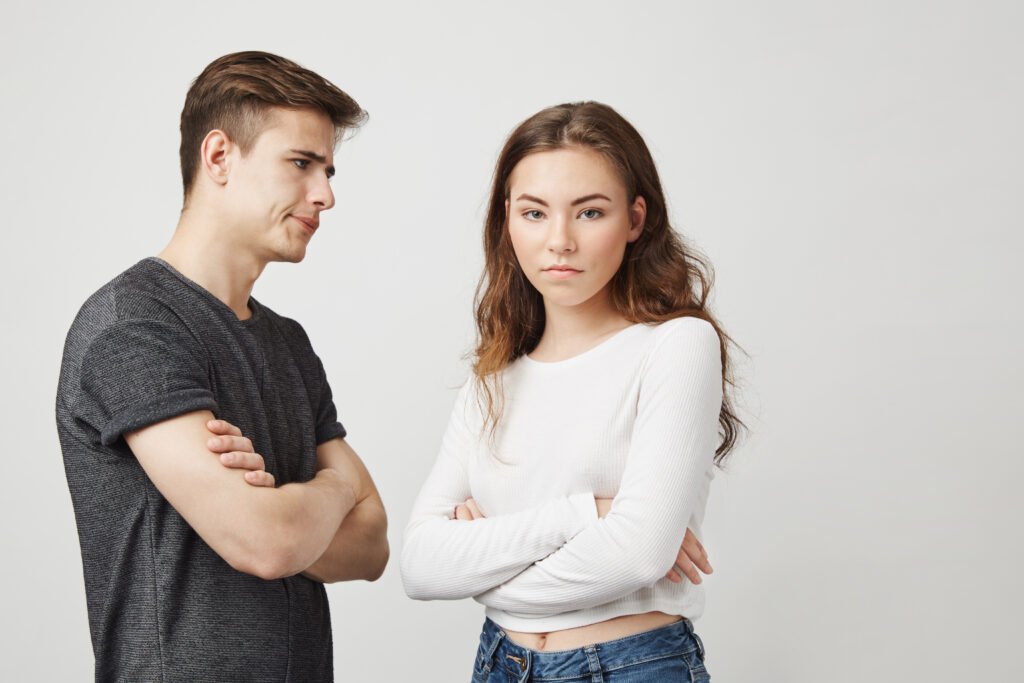 Controlling relationship dynamics shown by a woman with crossed arms and a partner displaying tense, watchful behavior