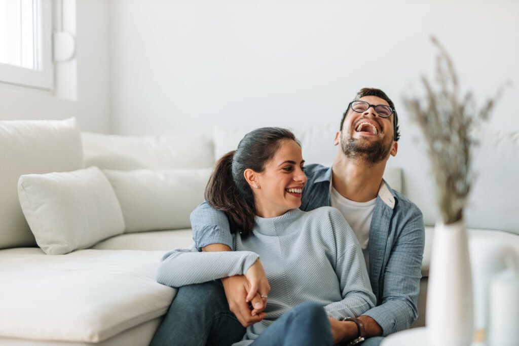 Couple laughing together on the couch, showing renewed marriage intimacy and emotional connection after reconnecting.