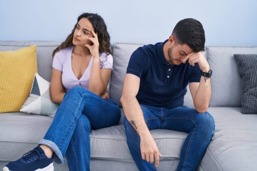 Couple sitting apart on a couch, showing tension and fading marriage intimacy during a complicated season.