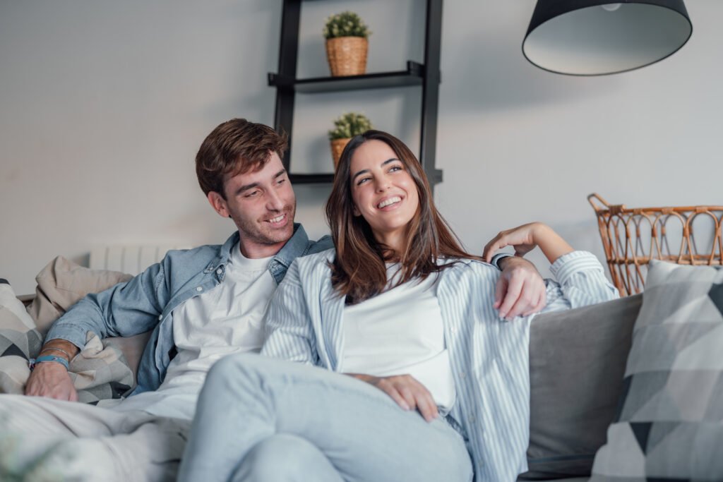 Couple smiling on a couch while reconnecting and rebuilding marriage intimacy through emotional connection.