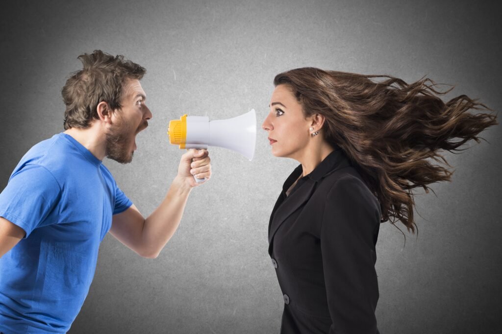 A man speaking aggressively through a megaphone toward a woman, illustrating emotional overwhelm and unhealthy communication dynamics in a relationship