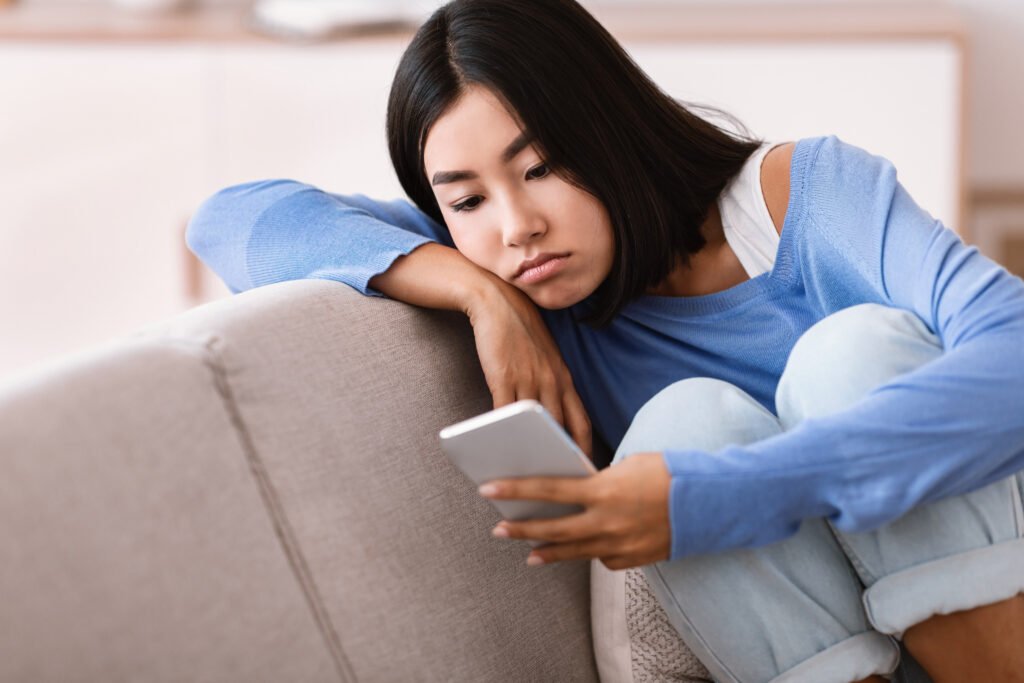 Woman sitting alone on a couch looking at her phone after a breakup